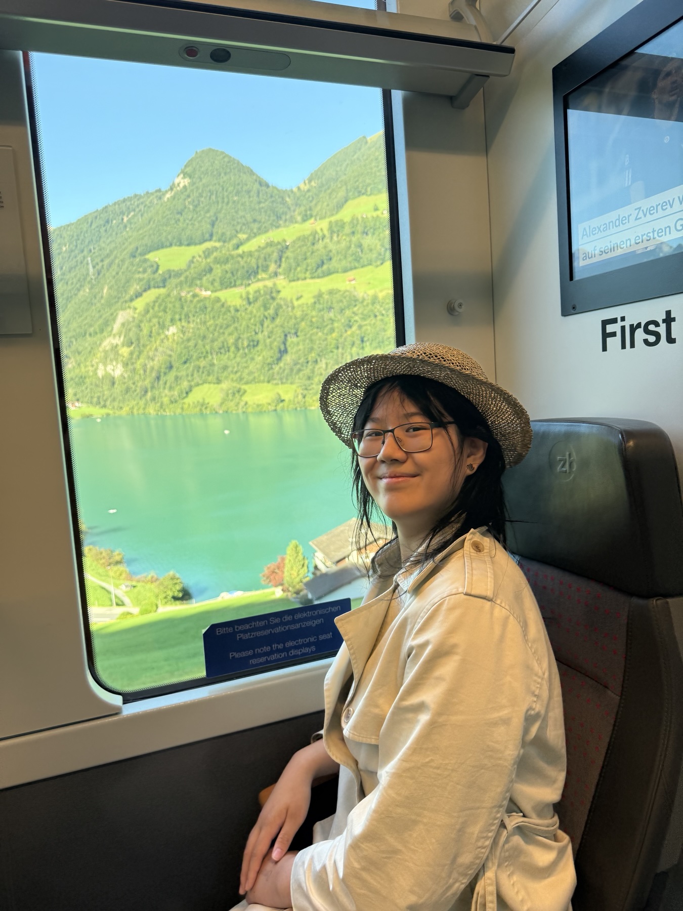 Ronova Deng seated by a train window, with a lake and green hills in the background.